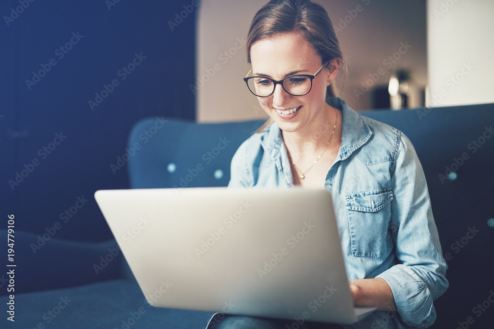 Smiling young female entrepreneur sitting on a sofa working online Smiling young female entrepreneur sitting on a sofa working online