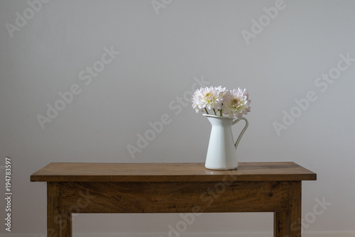 Fototapeta Naklejka Na Ścianę i Meble -  White dahlias in jug on wooden table against neutral wall background