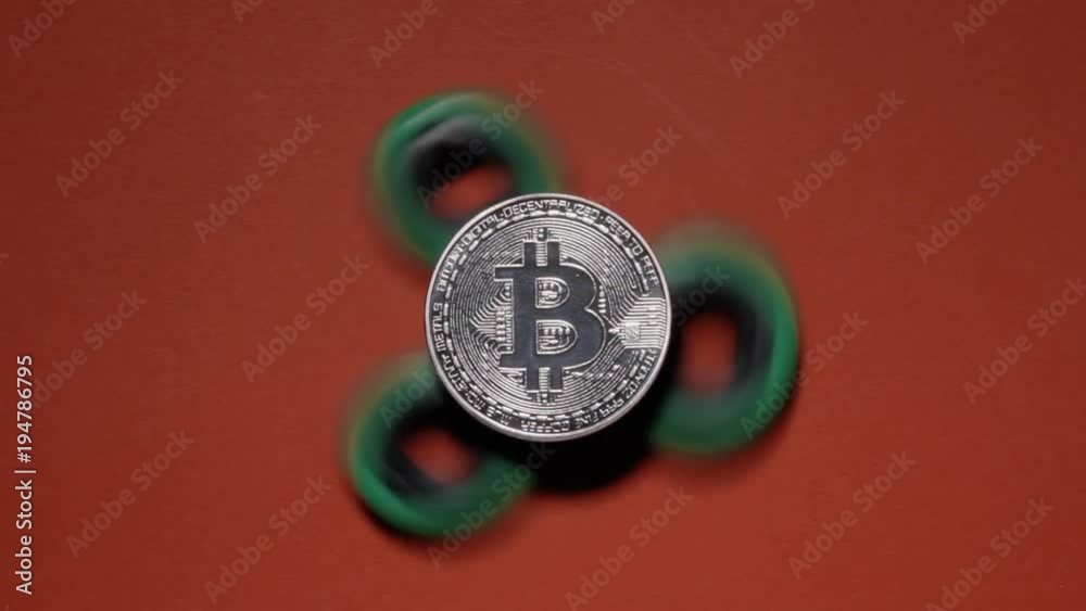 A silver bitcoin on a spinning toy, a hand stops it.
