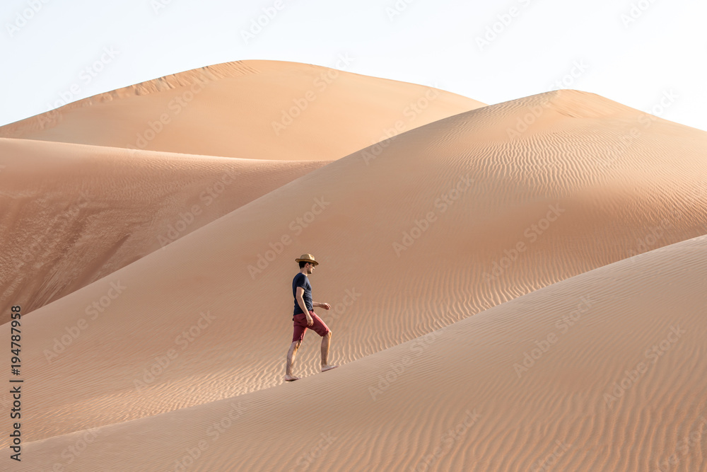 Young causasian male tourist in shorts hiking in giant Liwa desert dunes. Abu Dhabi, UAE.