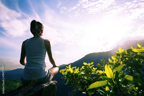 Young yoga woman at sunrise mountain peak cliff edge