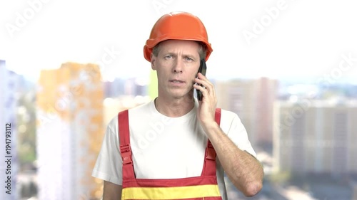 Mature construction engineer, blurred background. Middle-aged builder in hardat and uniform talking on his cell phone. People, repair, industry. photo