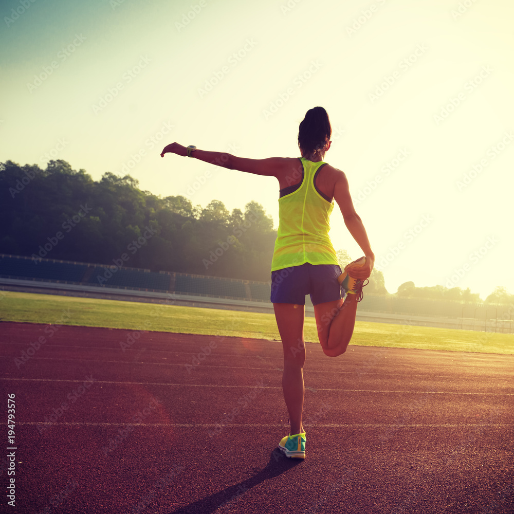 Young woman stretching legs before run during sunny morning on stadium