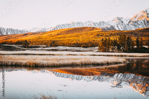 Mirror surface and peaks of the rocks of the lake in the mountain valley. The mountain range on the horizon under a colorful sky. Autumn weather