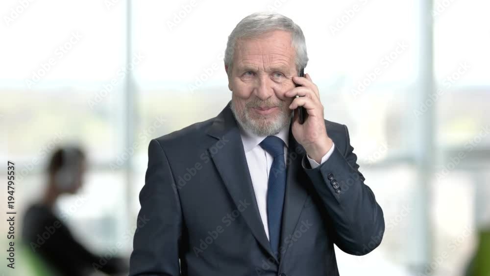 Elderly manager talking on cell phone. Senior man in formal wear using his smartphone on office background. Businessman talking on phone with partners. Elderly manager talking on cell phone. Senior man in formal wear using his smartphone on office background. Businessman talking on phone with partners.