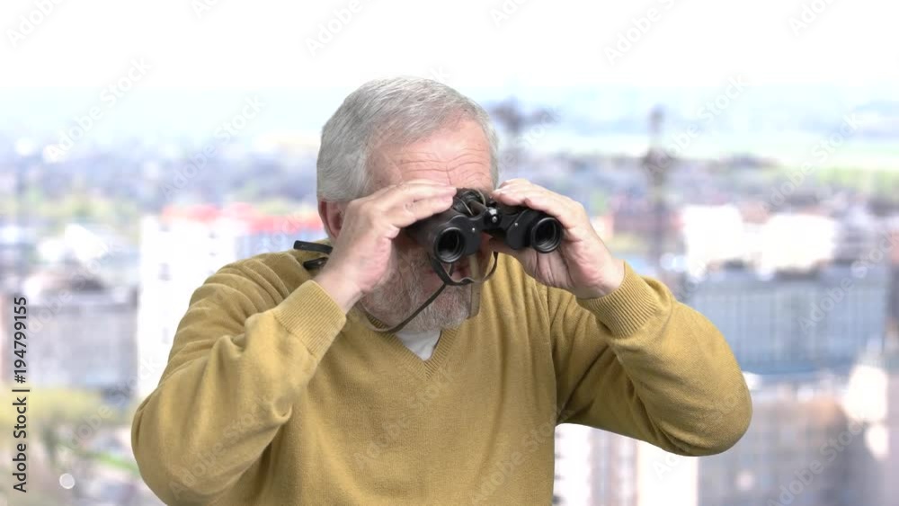 Aged man with pair of binoculars. Senior bearded man looking through binoculars on blurred background. Travel and exploration concept. Aged man with pair of binoculars. Senior bearded man looking through binoculars on blurred background. Travel and exploration concept.