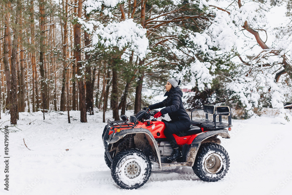 Fototapeta premium young girl on a motorcycle rides in snow-covered pine forest in winter