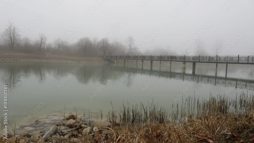 Amazing landscape of bridge reflect on surface water of lake, fog evaporate from pond make romantic scene or Beautiful bridge on lake with trees at fog. Iron bridge over lake in misty morning. Slider 