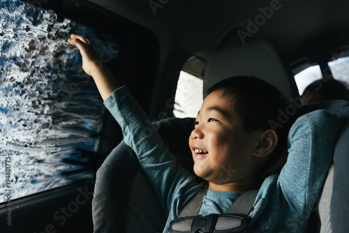Little Asian boy smiling out car window inside car wash photo
