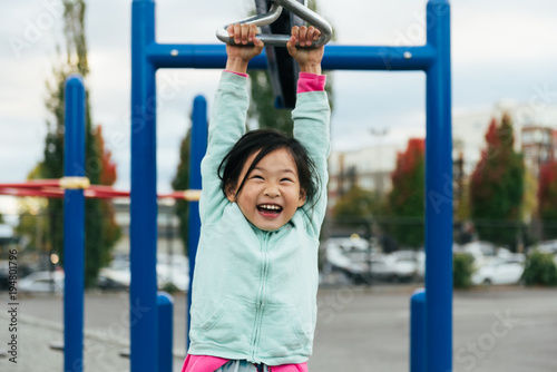 Chinese American girl with large smile rides zip line on playground structure