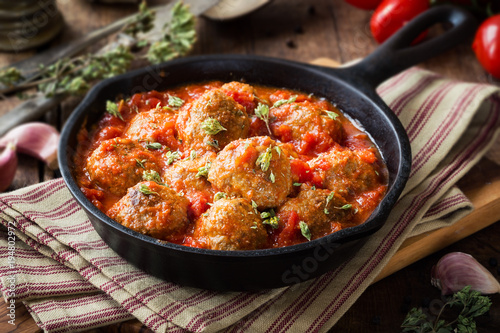 Meatballs in tomato sauce with dried oregano in a rustic vintage cast iron skillet photo