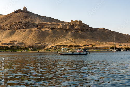 Small motor boat for tourists on the Nile River in Cairo (Egypt), in the background ruins of an ancient Arab town in the desert. The tomb of the Aga Khan