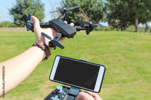 Young man with remote control cell phone hold drone. Sunny green nature