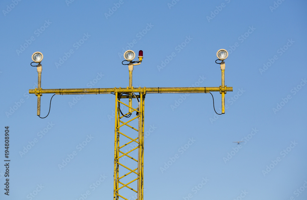 Airport landing lights against a blue sky. Airplane in the background out of focus. Airport landing lights against a blue sky. Airplane in the background out of focus.