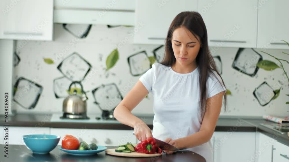 Pretty young woman prepares lunch and shreds green cucumber for salad with sharp knife Pretty young woman prepares lunch and shreds green cucumber for salad with sharp knife
