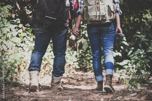 Closeup image of a lover couple holding hands and trekking in a tropical forest together