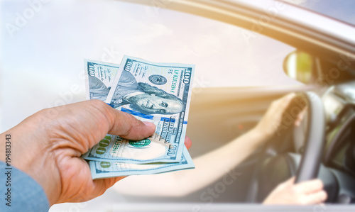 Business woman hand holding American dollar Currency isolated on blurred woman driving car with blue sky, insurance concept