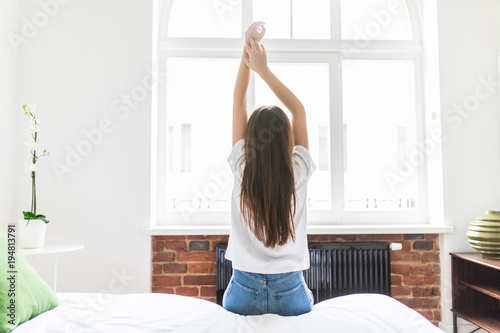 Woman stretching in bed after wake up, back view. Young woman in her morning bed.