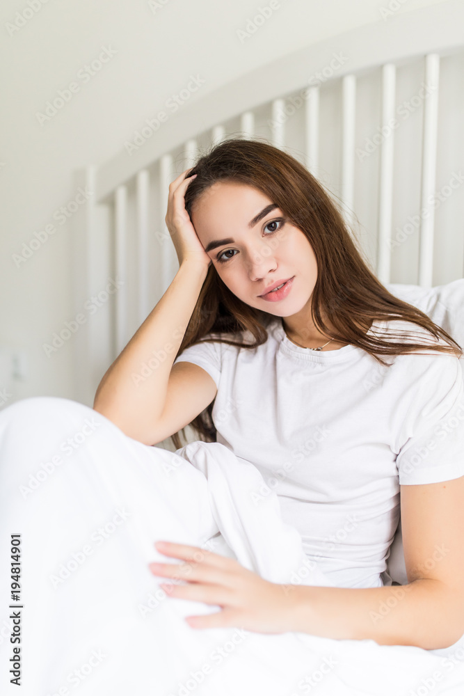 Attractive young woman is smiling and looking at the camera while sitting in bed under the blanket Attractive young woman is smiling and looking at the camera while sitting in bed under the blanket