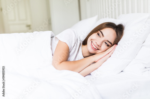 Smiling casual brunette lying in her bed in bright bedroom before sleep