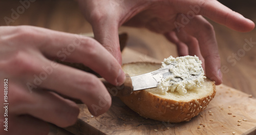 man hands spreading cream cheese on sesame bun on wood board
