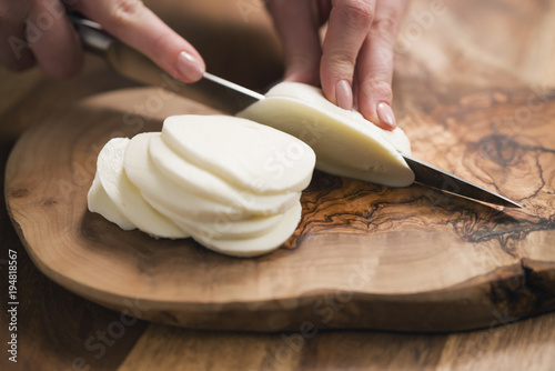 female teen hand slicing mozzarella cheese with knife on wooden board