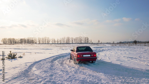 A red car is standing on a snowy road during sunset