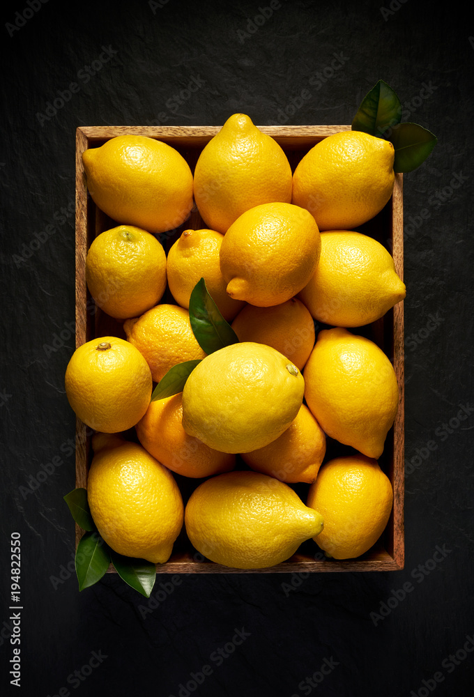 Fresh lemons in a wooden container on a black stone background, top view