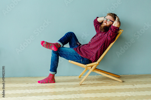 Dreaming about vacation concept. Studo shot of man resting on a chair over gray wall at home. photo
