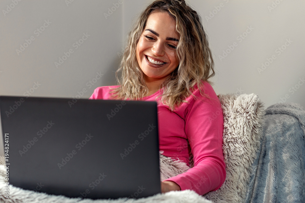 Smiling casual beautiful woman working on a laptop sitting on the bed in the house. Freelance concept. Smiling casual beautiful woman working on a laptop sitting on the bed in the house. Freelance concept.