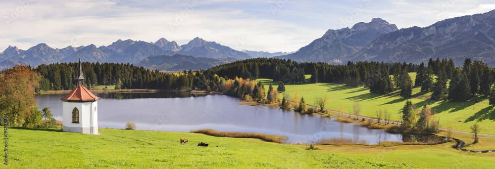 panoramic landscape in region Allgaeu with little chapel at lake and alps mountain range