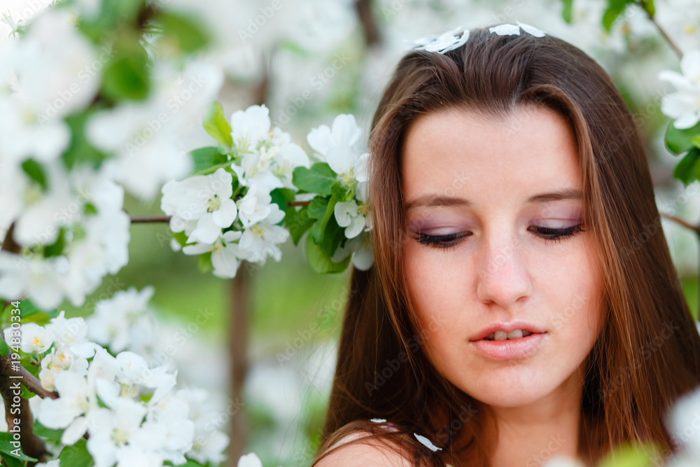 Portrait of a young beautiful woman posing among blooming Apple trees. Girl with long hair posing among the flowers. Close-up with space for text.