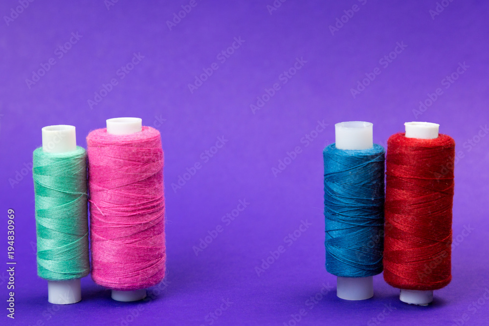 Several reels with threads on a blue background. The thread is stretched between the multi-colored thread coils. Several reels with threads on a blue background. The thread is stretched between the multi-colored thread coils.
