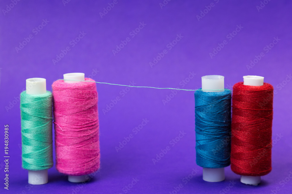 Several reels with threads on a blue background. The thread is stretched between the multi-colored thread coils. Several reels with threads on a blue background. The thread is stretched between the multi-colored thread coils.
