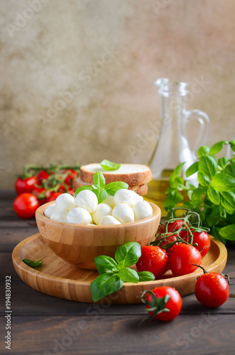 Italian food ingredients     mozzarella  tomatoes  basil and olive oil on rustic wooden table.