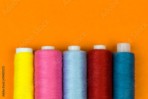 The coils with threads stand vertically on an orange background. A row of coils with bright colored threads standing.