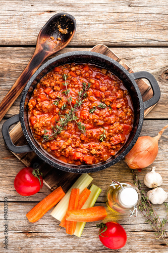 classic italian bolognese sauce stewed in cauldron with ingredients on wooden table, top view