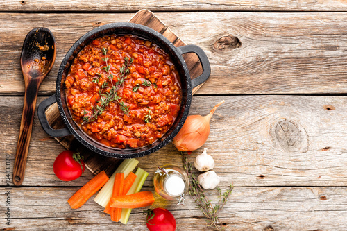classic italian bolognese sauce stewed in cauldron with ingredients on wooden table, top view, culinary background with space for text