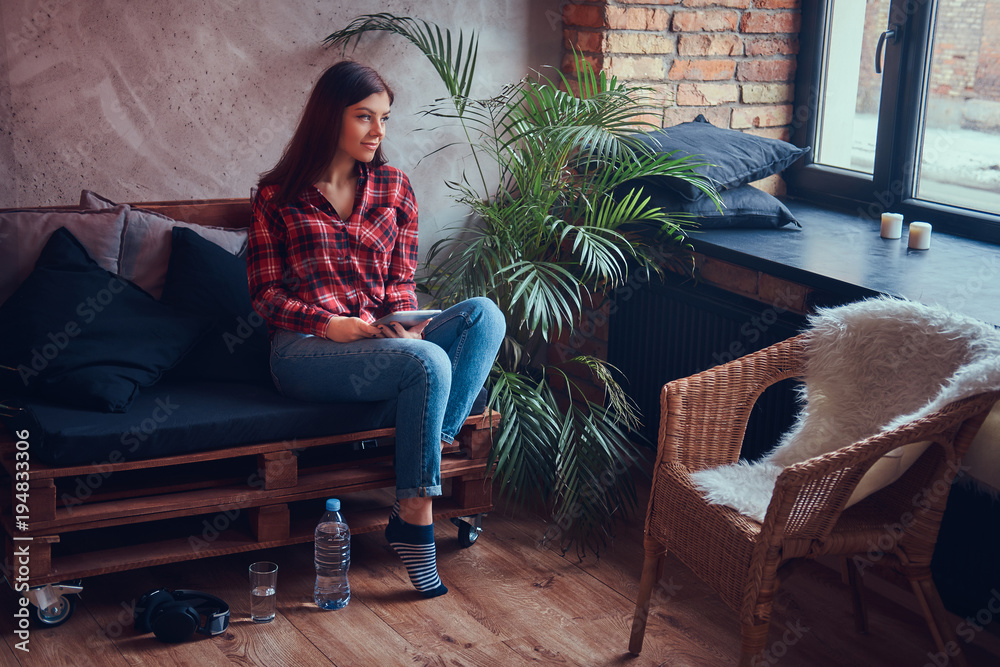Obraz premium Charming brunette in a flannel shirt and jeans sitting on a couc
