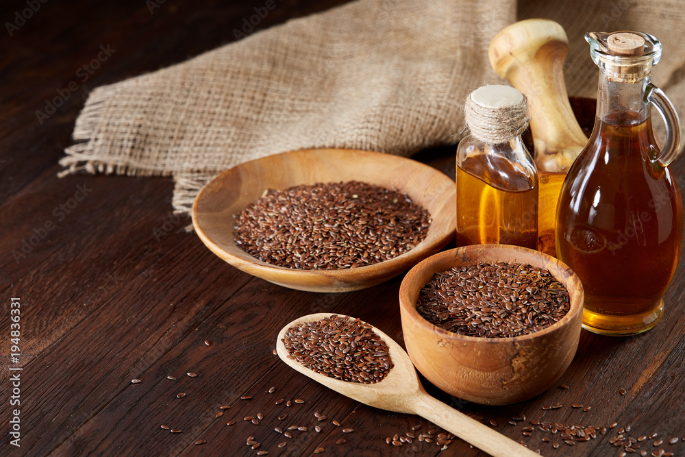 Flax seeds in bowl and flaxseed oil in glass bottle on wooden background, top view, close-up, selective focus