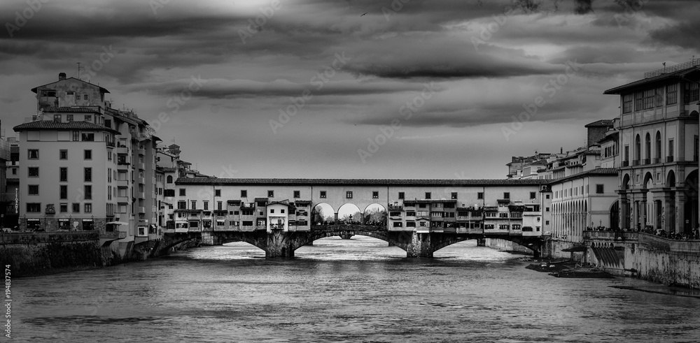 Beautiful black and white photo of the Ponte Vecchio, a medieval stone arch bridge over the Arno River, in Florence, Italy.