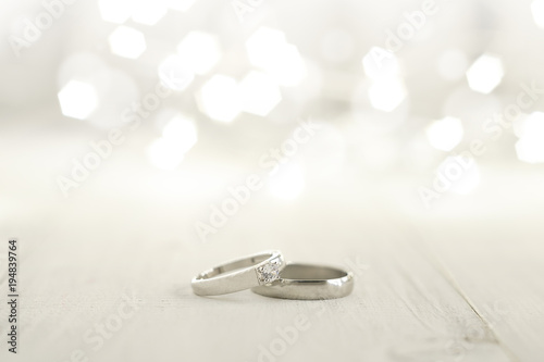 Two wedding rings place on wooden floor with light bokeh background.