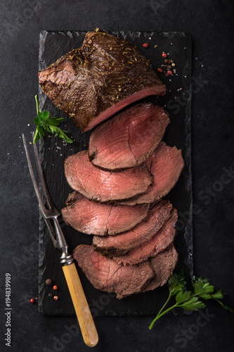 Photos sliced  roast beef on slate board, black background