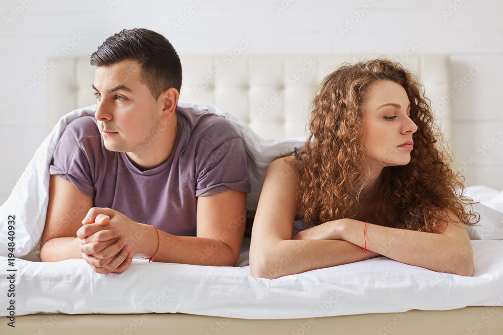 Thoughtful discontent young woman and man don`t look at each other, have quarrel and sort out their relationships, lie on comfortable bed. Newlyweds in bedroom being in bad mood at morning Thoughtful discontent young woman and man don`t look at each other, have quarrel and sort out their relationships, lie on comfortable bed. Newlyweds in bedroom being in bad mood at morning