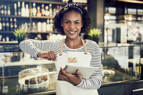 Smiling African entrepreneur standing in her cafe with a tablet