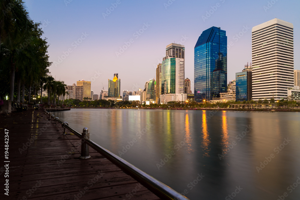 Wooden walkway in the park with a view of the building in the background and the lights reflected in the lake.