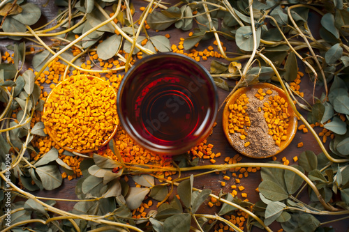 Close up of Fenugreek with its seeds and powder and the extracted water on a wooden surface in dark Gothic  colors. photo