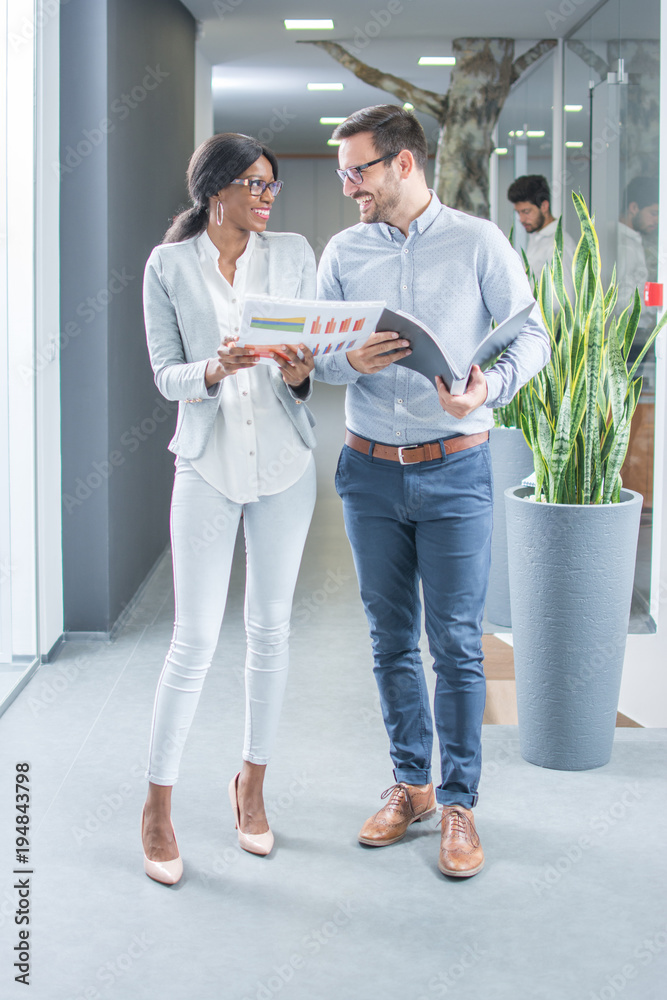 Full length portrait of two smiling business people with documents talking in office hallway. Full length portrait of two smiling business people with documents talking in office hallway.