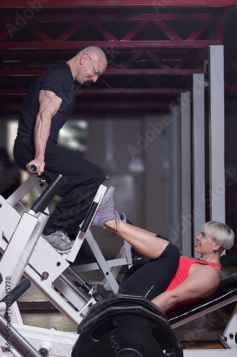 A woman and a man on the leg press at the fitness club having a good time and smiling to each other.