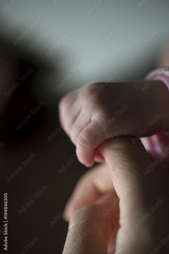 Newborn small hand holding mature finger